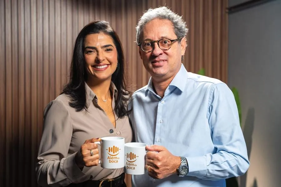 Apresentadora e convidado com canecas no podcast Além da Boca
