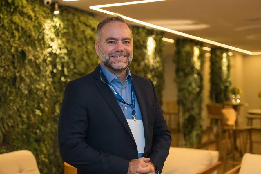 Executivo de terno sorrindo diante de parede de plantas em evento da Allianz