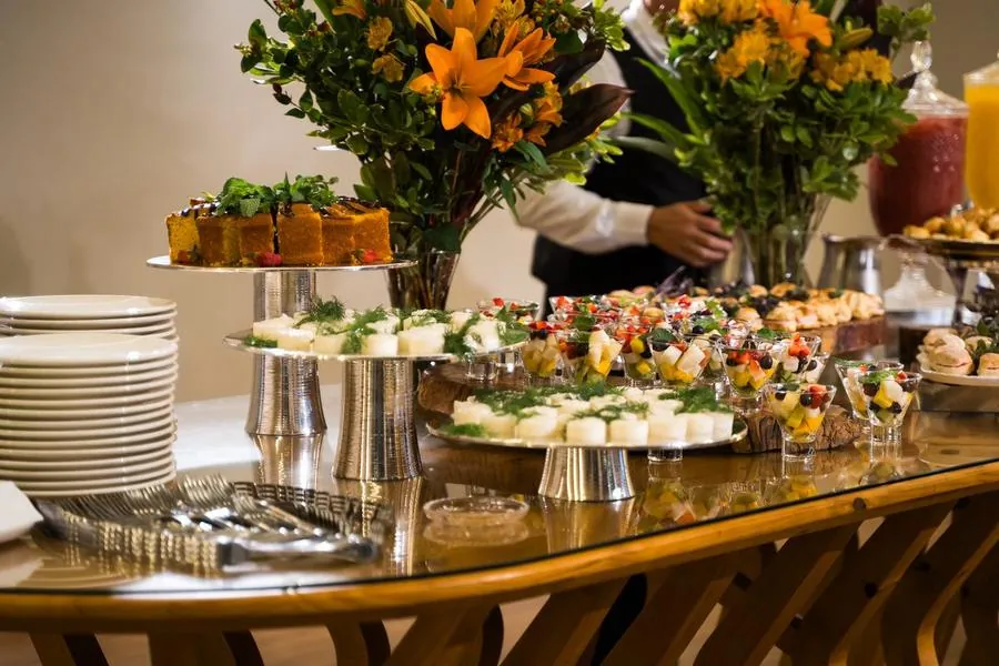 Mesa de buffet com frutas, folhagens e arranjos de flores em evento