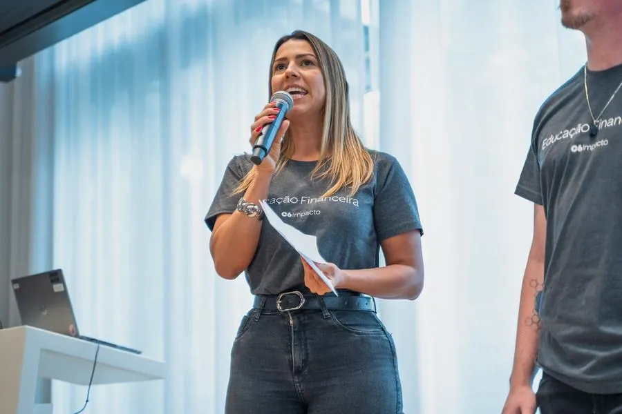 Apresentadora com microfone e anotações no evento C6 Impacto