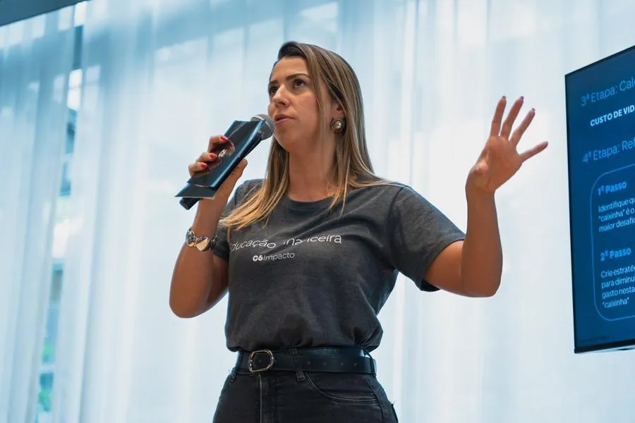 Apresentadora falando ao microfone ao lado do telão no C6 Impacto