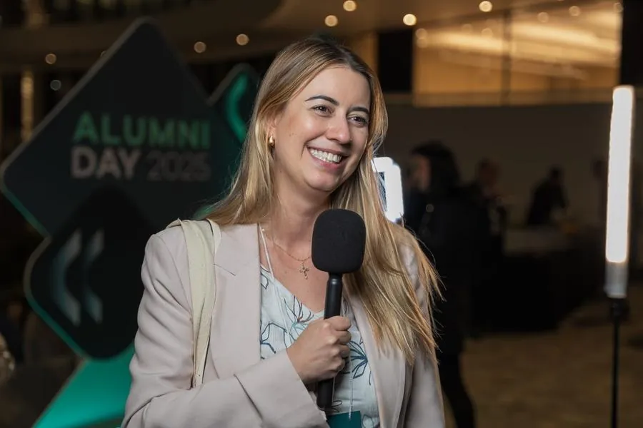 Repórter com microfone sorrindo no Alumni Day do Einstein