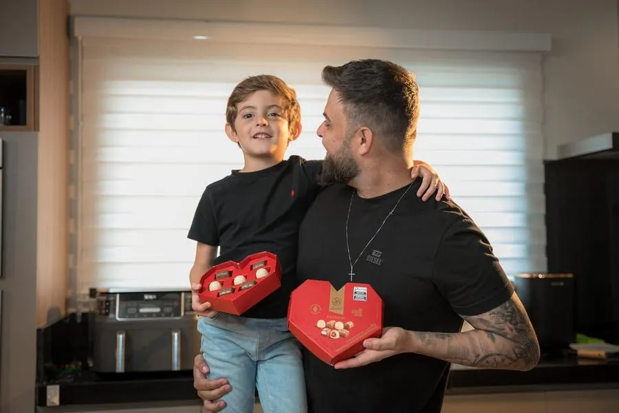 Pai e filho segurando caixas de coração da Sodiê Doces na cozinha