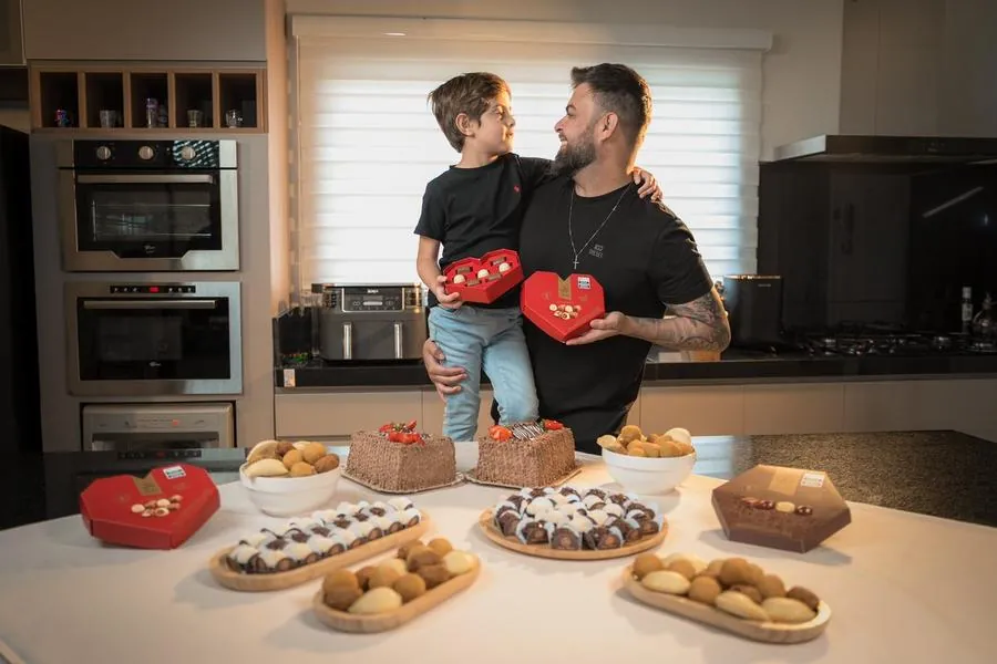Pai e filho com mesa de doces e salgados da Sodiê Doces na cozinha