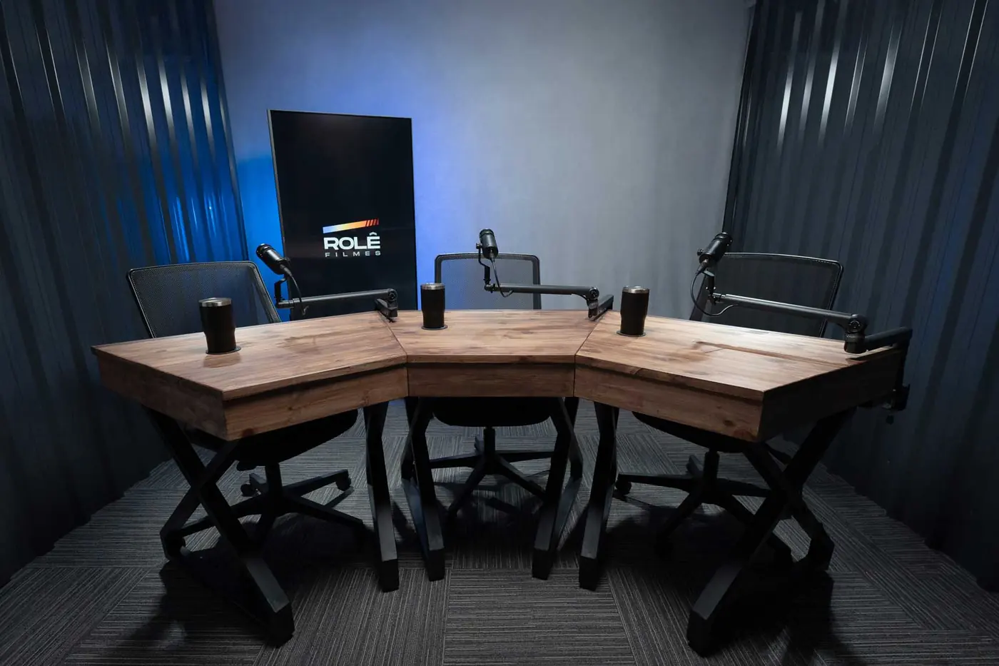 Mesa de podcast com microfones Shure e iluminação azul no estúdio da Rolê Filmes