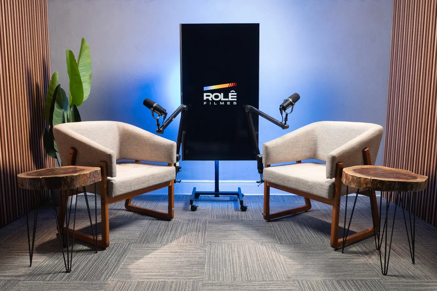 Sala de poltronas do estúdio de podcast com iluminação azul, duas poltronas e microfones Shure profissionais