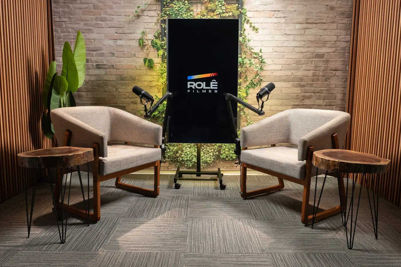 Sala de poltronas do estúdio de podcast da Rolê Filmes em São Paulo, com parede de tijolos, plantas e microfones Shure